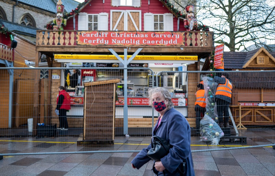 A woman wearing a face mask looks to the camera as workers remove decorations from Christmas markets