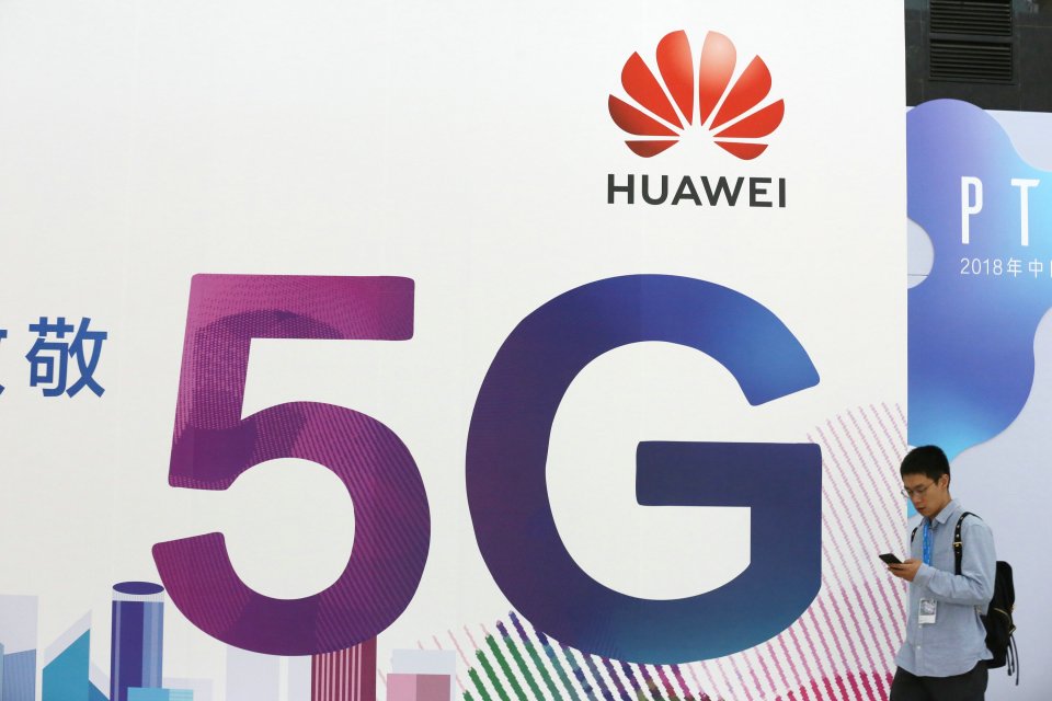 People walk past the stand of Huawei featuring 5G technology during the PT Expo China at Beijing National Convention Center on September 26, 2018