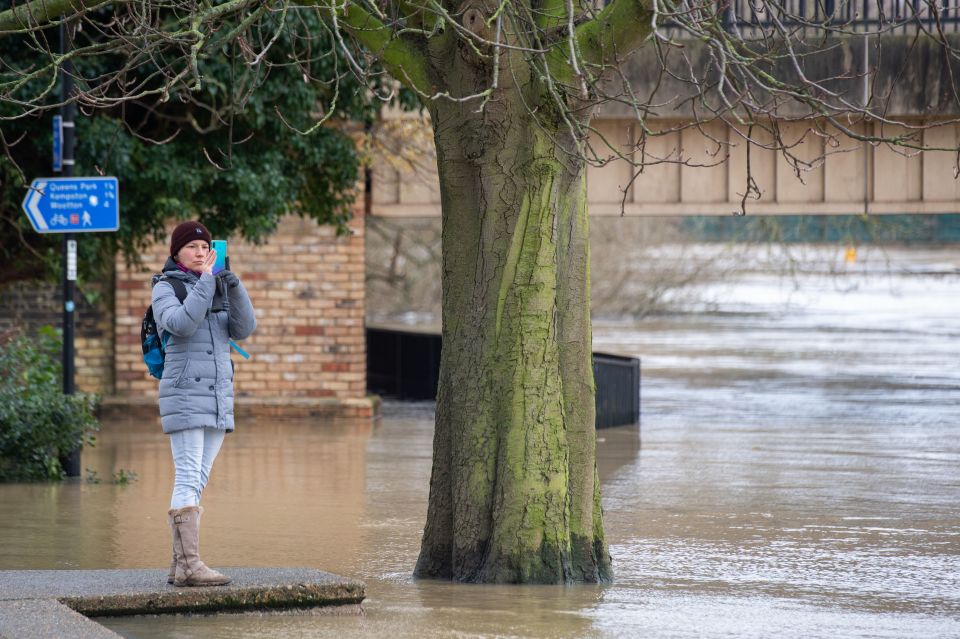 A woman takes a photo of flooding in Bedford