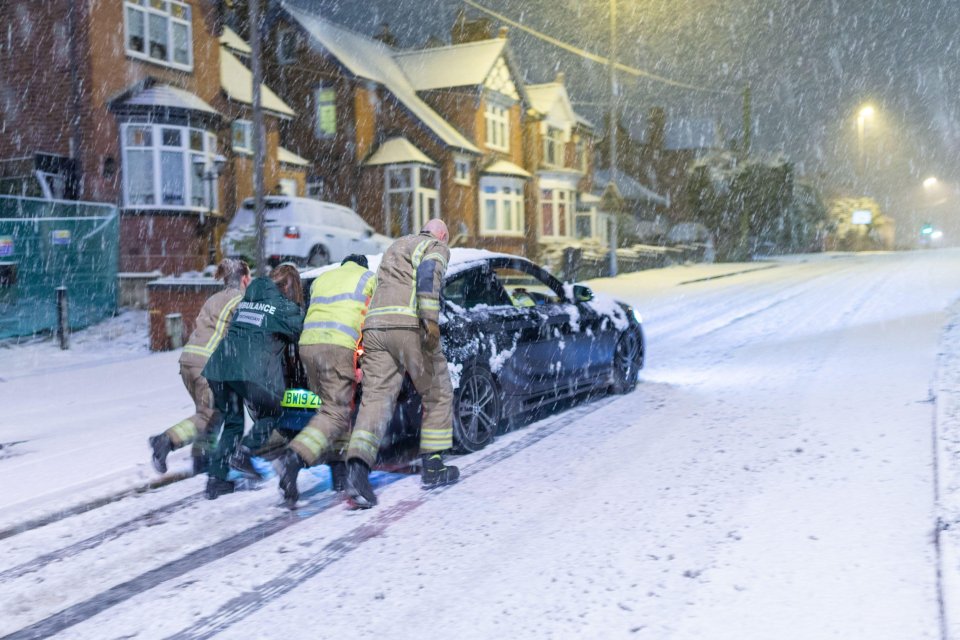 Ambulance and fire crew work to push a stranded car up a road in Cradley Heath, West Midlands