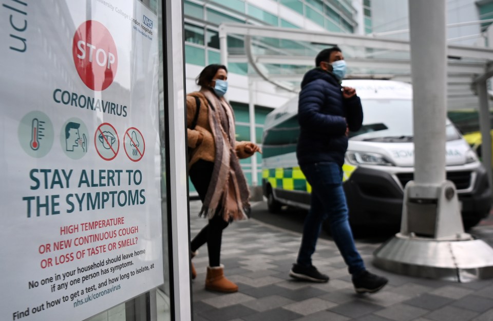 Masked up people walking by warning signs in London