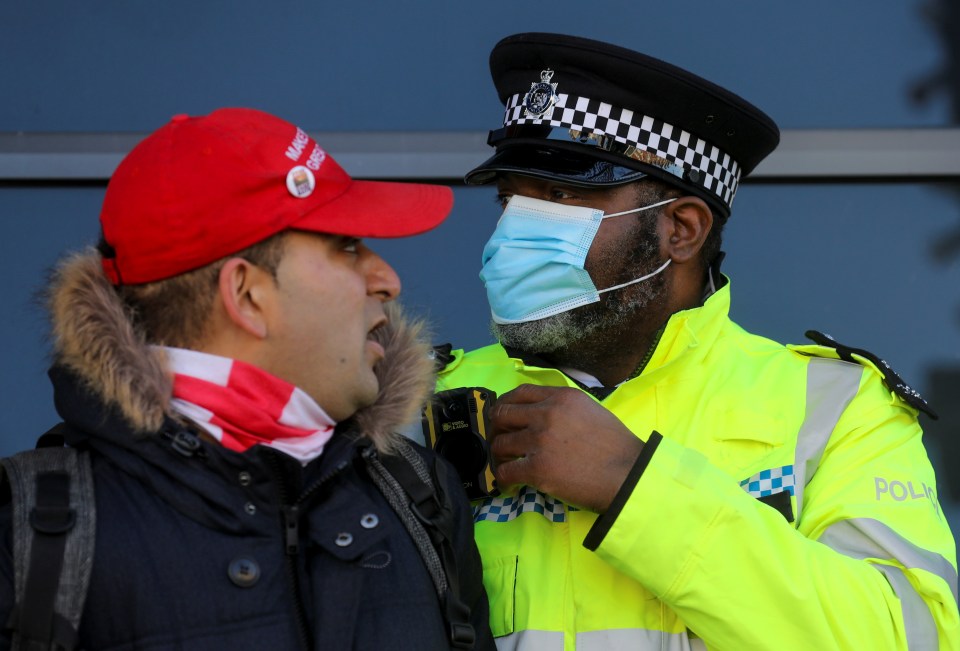 A masked officer leads away a man with the hat reading 'Make Britain Great Again'