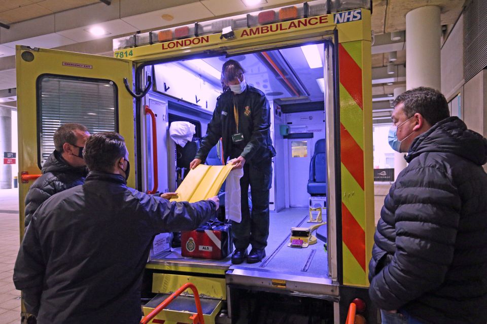 Metropolitan Police officers in plain clothes are shown around the rear of an ambulance by a member of the London Ambulance Service