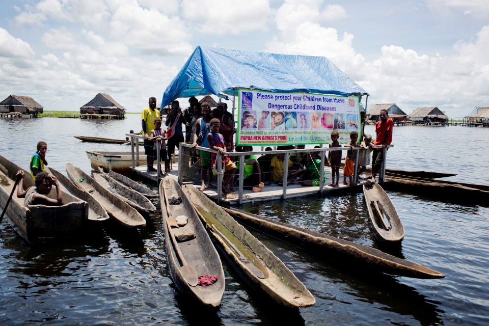 Families congregate at a mobile clinic in Kambaramba village to have their children vaccinated against polio, having travelled in dugout canoes in 2019