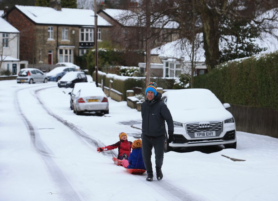 A man pulls children on a sledge over a snow-covered road in Sheffield