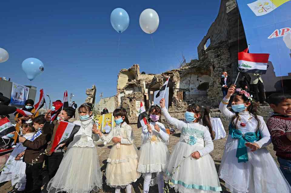 Children dressed in costumes wave national flags in the ruins of the Syriac Catholic Church