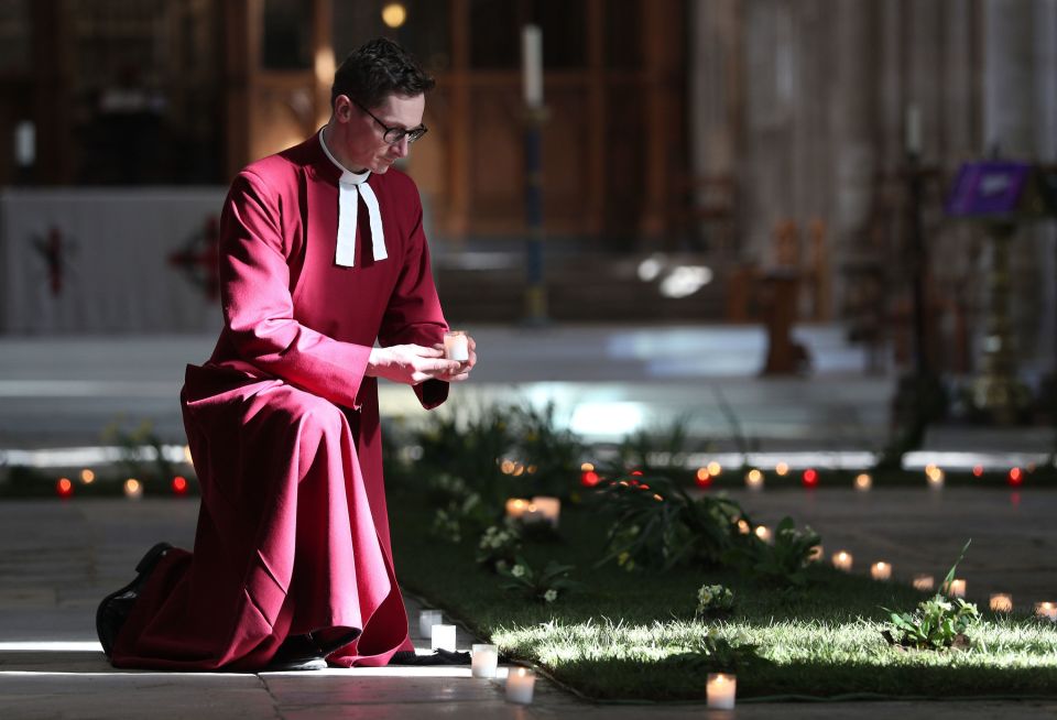 Reverend Canon Andrew Trenier holds a candle next to a green meadow cross in the Nave of Winchester Cathedral ahead of the National Day of Reflection