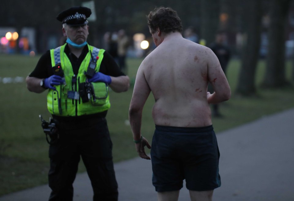 Cops speak to a bloody and bruised man as darkness falls in Hyde Park, Leeds