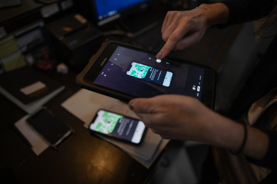 An employee takes a photo of phone screen that shows the green passport, part of the check-in procedure at Herods Hotel