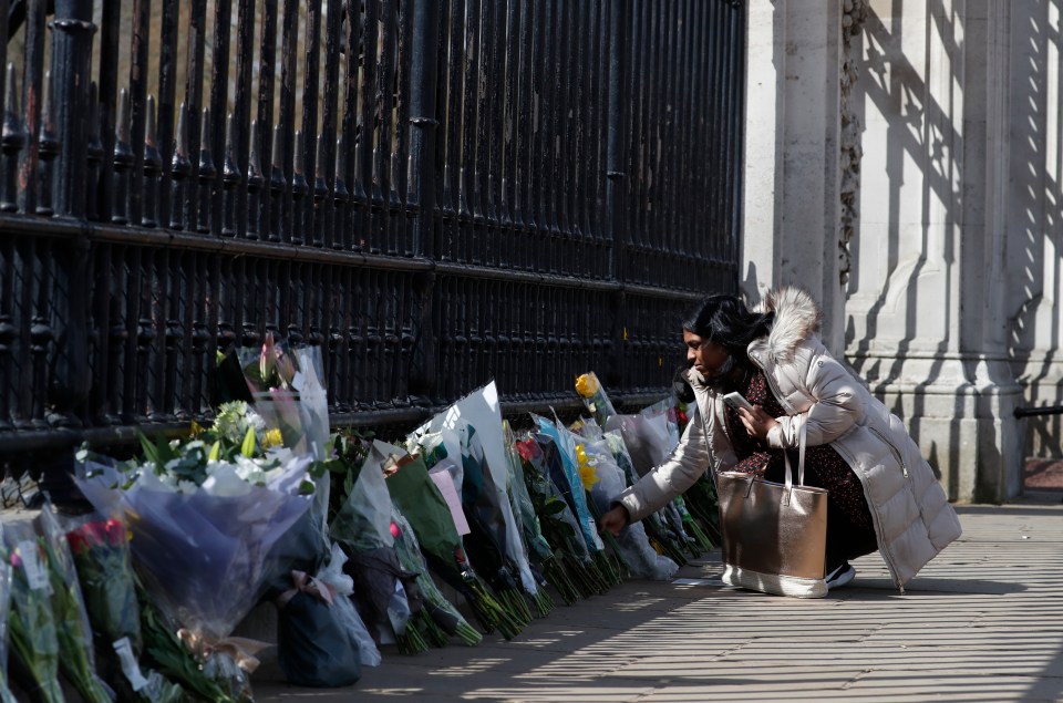 A woman places flowers in front of the gate at Buckingham Palace following the announcement that Prince Philip has died