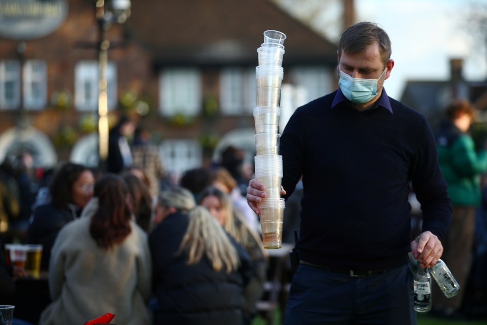 A man carries used plastic cups and bottles at The Fox on the Hill pub in London