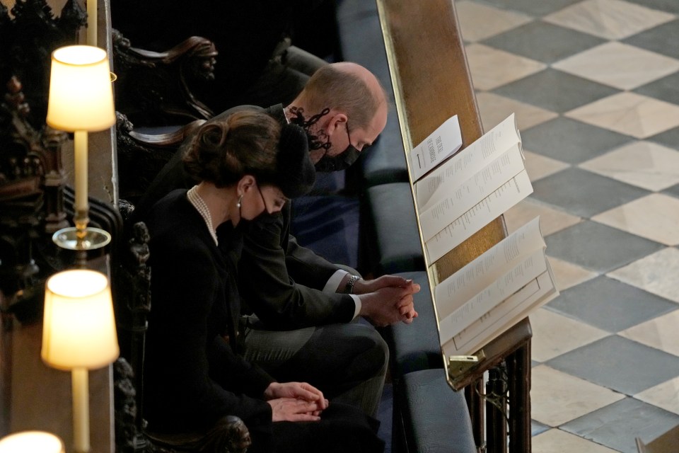 Prince William and Kate sitting with bowed heads and wearing masks