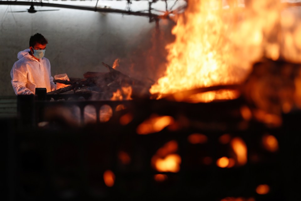 A frontline worker ignites a funeral pyre of a coronavirus patient