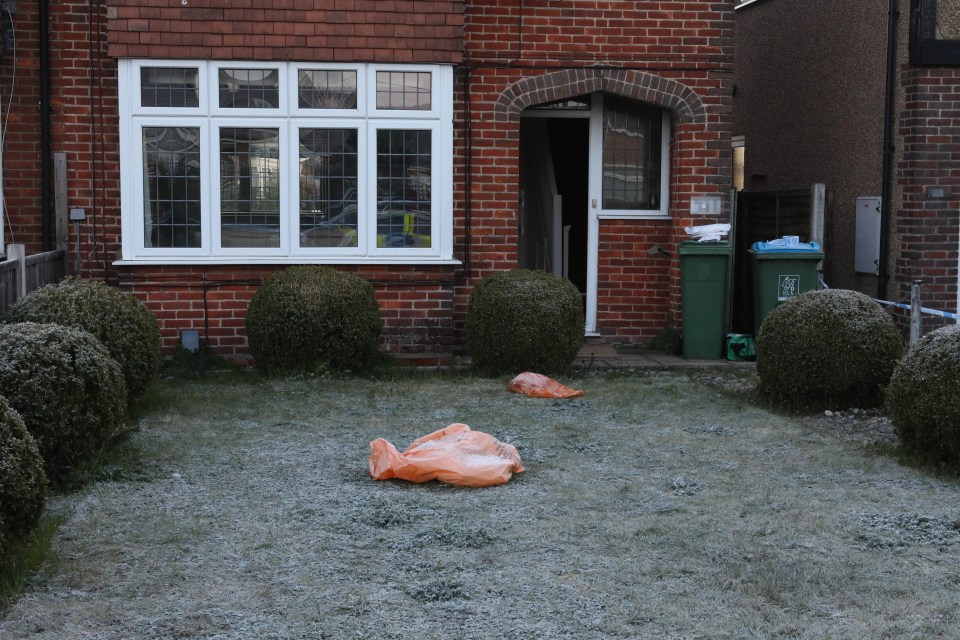 Orange bags, possibly containing evidence, are seen on the lawn in front of the property