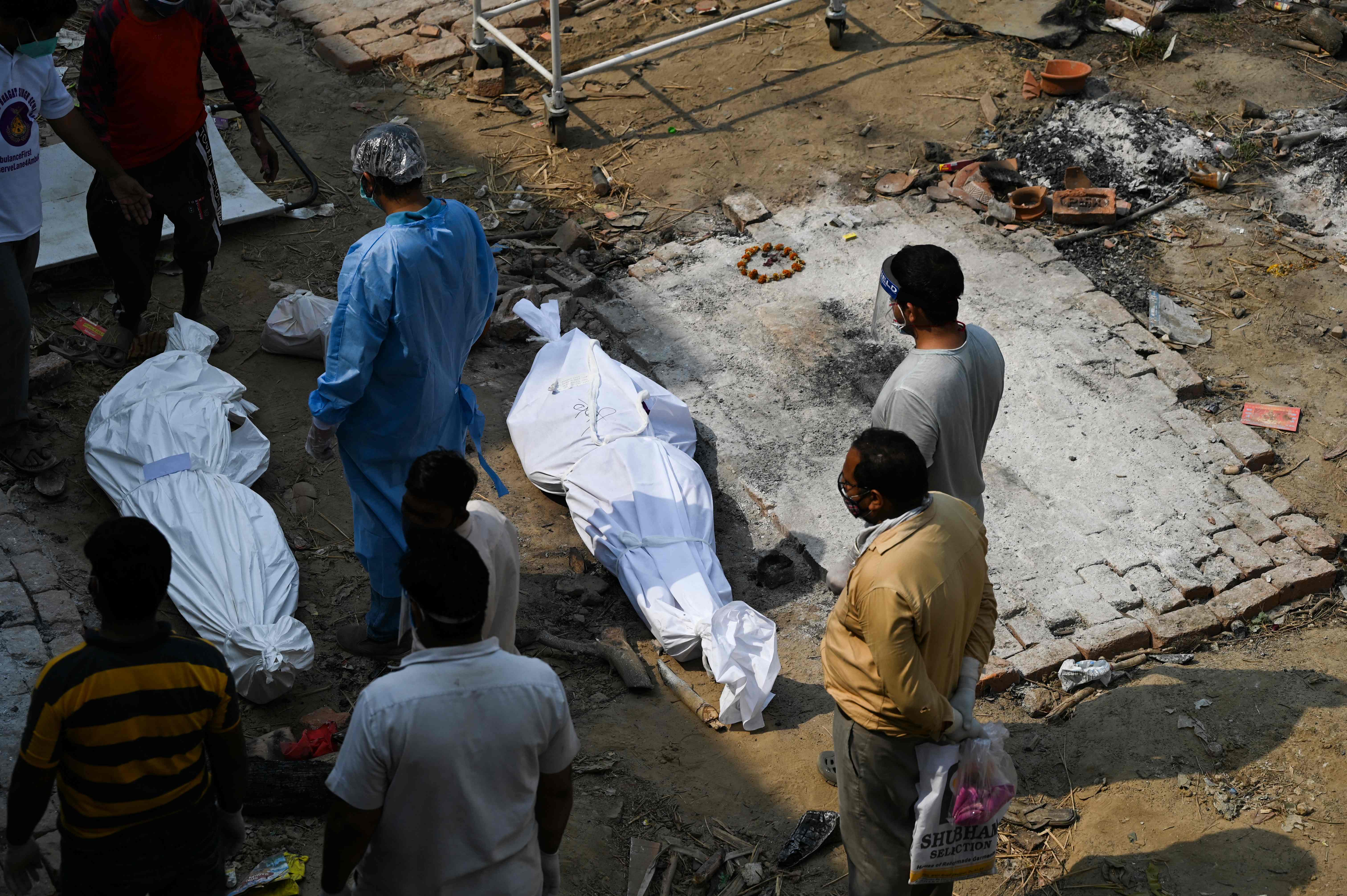 Relatives stand next to the  body of a victim who died from Covid at a cremation ground in New Delhi