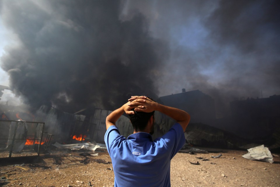 A man stands near a burning sponge factory after it was hit by Israeli artillery shells