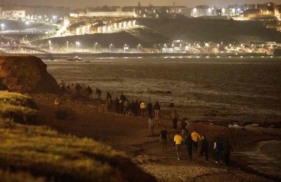 Moroccan migrants walk along the shore towards the northern town of Fnideq as they attempt to cross the border from Morocco to Spain's North African enclave of Ceuta