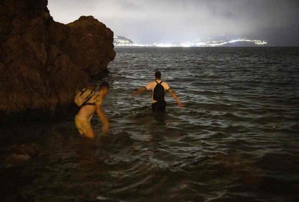 Moroccan migrants walk into shallow waters on the shore of the northern town of Fnideq