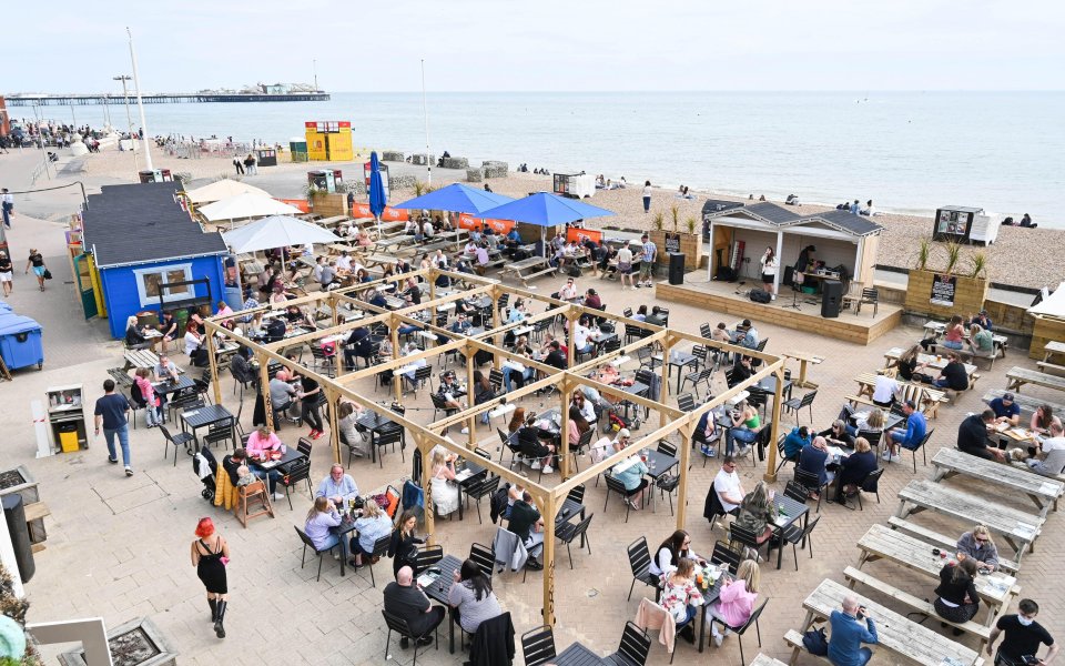 Visitors enjoy a warm day at Brighton seafront bars as people start to arrive for the Bank Holiday weekend