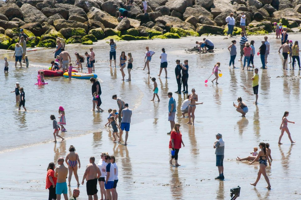 The beach is packed with families and sunbathers enjoying the sunshine and cooling off in the sea