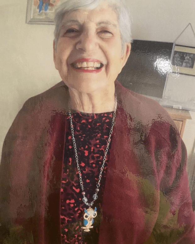 Smiling woman wearing a maroon cardigan and an owl necklace.