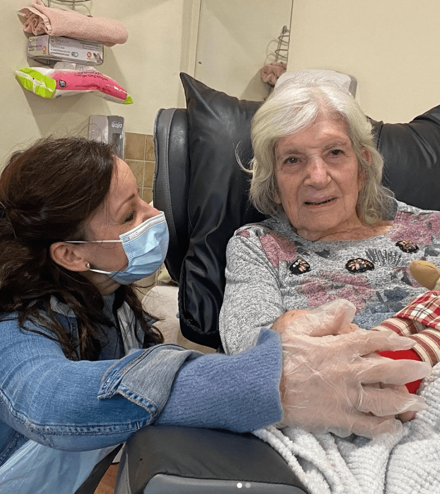 A woman wearing a face mask holds an elderly woman's hand.