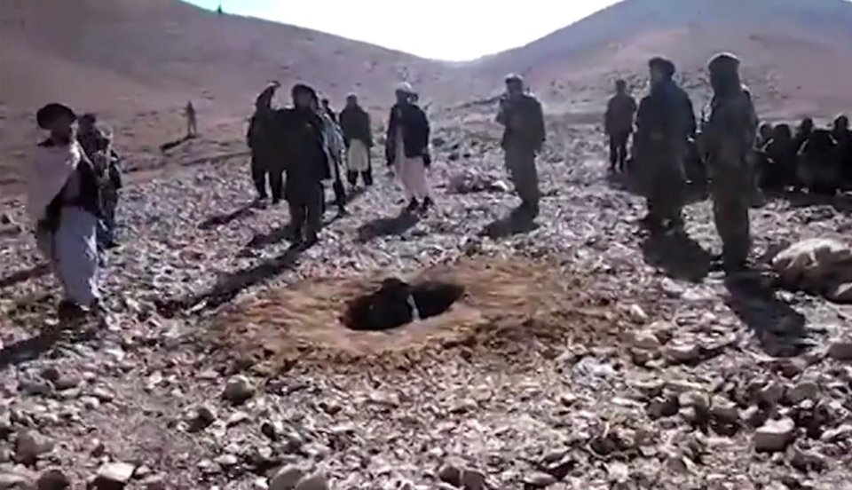 A woman sits in a shallow grave as Taliban fighters prepare to stone her in a vile execution