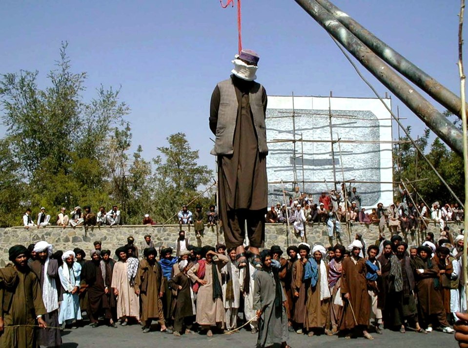 Hundreds of Afghan people gather round a man hanged by the Taliban in 2000