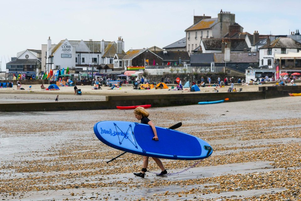 A paddle boarder walking across the beach at the seaside resort of Lyme Regis in Dorset