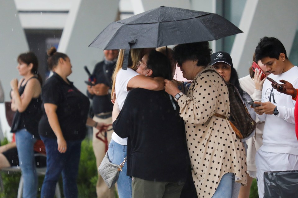 People embrace under an umbrella as authorities take residents to a community centre in Miami