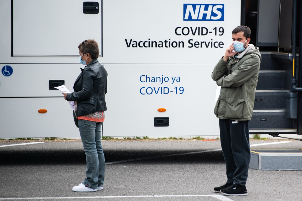 People queue outside a Covid vaccination bus at Bolton Cricket Club in Greater Manchester