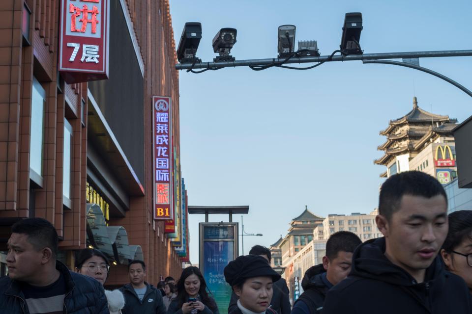 Pedestrians walk below CCTV cameras in Wangfujing Street in Beijing, China