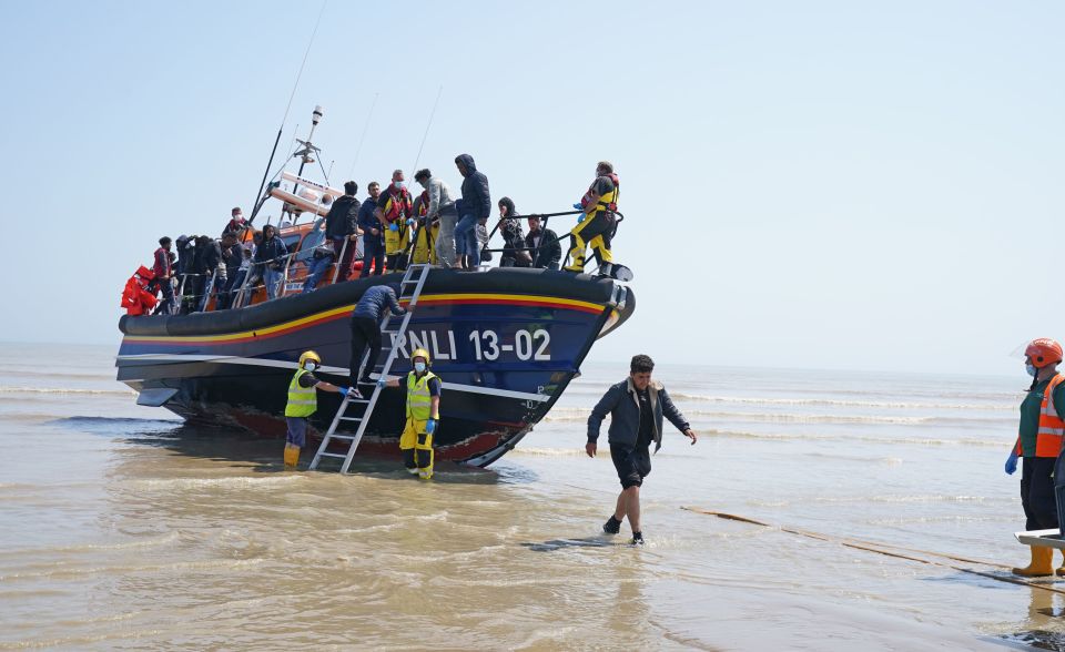 People thought to be migrants make their way up the beach after arriving on a small boat at Dungeness in Kent