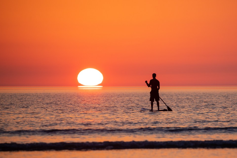 A stand up paddle boarder watches the sunset over the North Devon coast as the heatwave continues across the UK