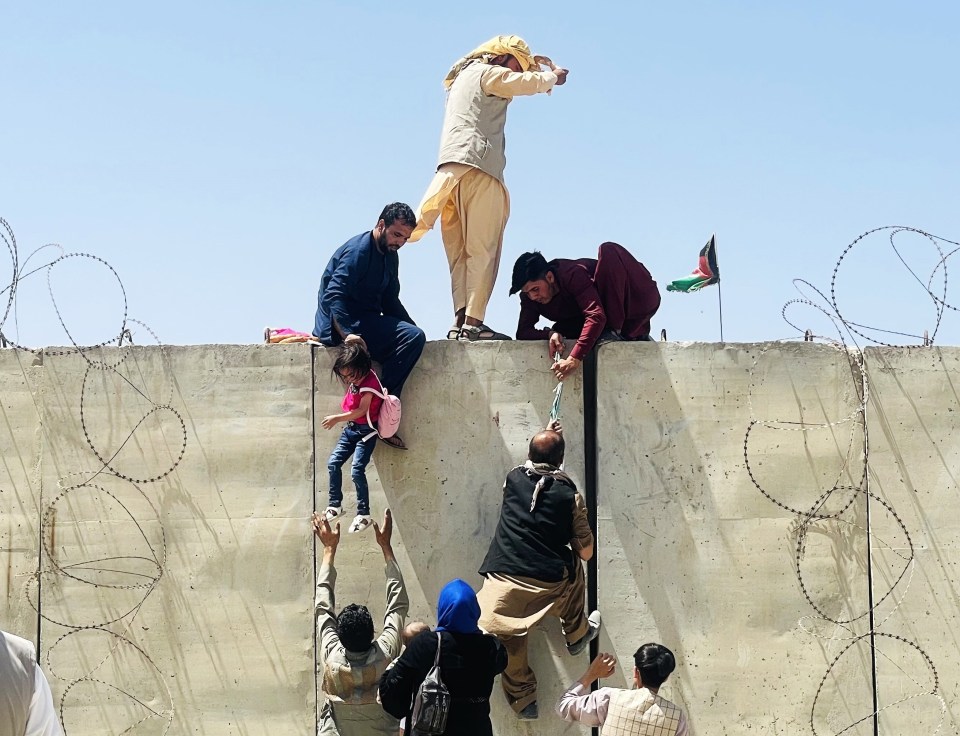 Desperate Afghans climb a wall at Kabul airport