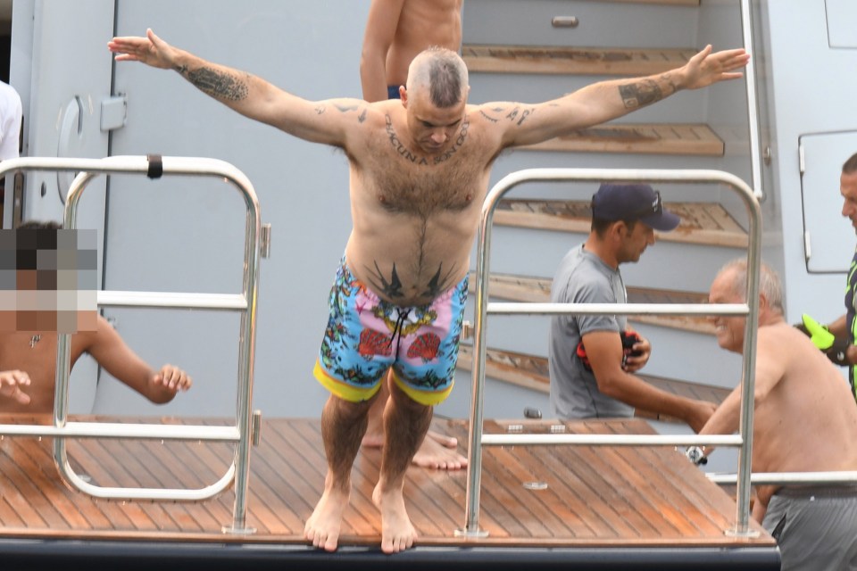 Robbie Williams strikes an Angelic pose before diving head-first into the water