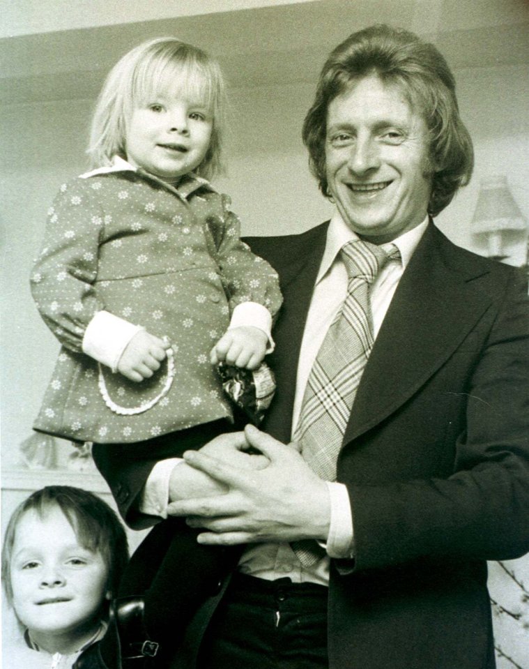 Black and white photo of a man holding a young girl, with another young child visible in the foreground.