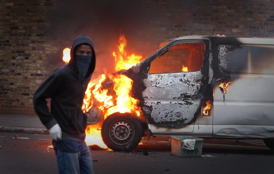 A rioter in front of a burning van in London