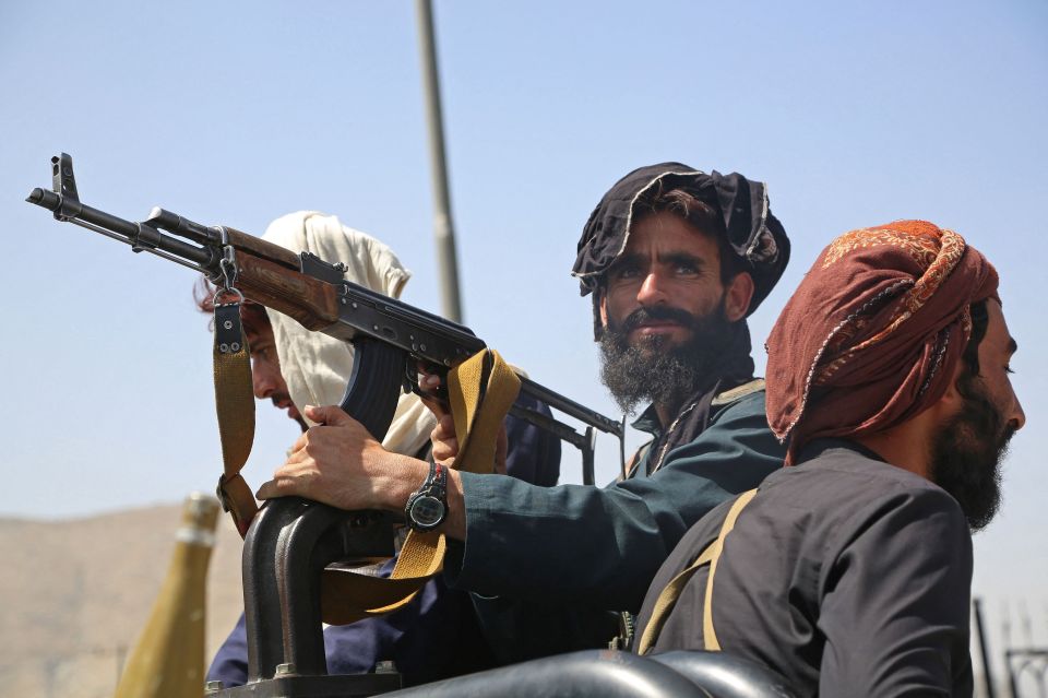 Taliban fighters stand guard in a vehicle along the roadside