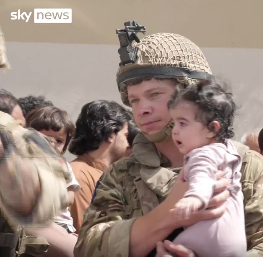 A soldier grips a child as parents try to get their child out of the country