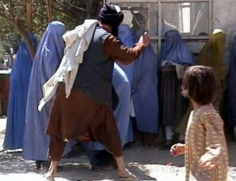 Taliban fighter strikes a group of women with a rod as a child watches on