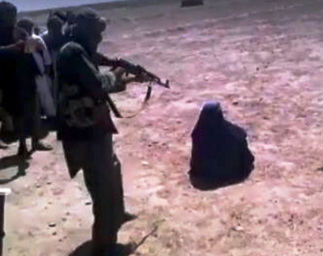 A woman sits before a Taliban fighter armed with an AK-47 in 2016