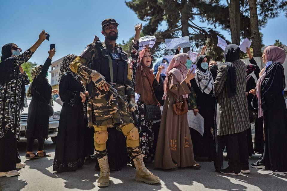 Protesters shout as a Taliban fighter stands guard