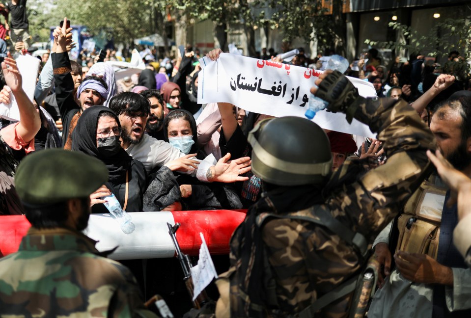 Taliban soldiers stand in front of protesters