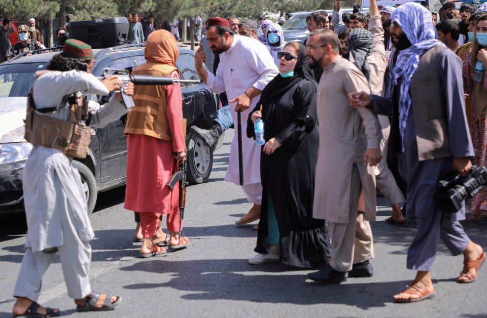 A Taliban fighter aims his gun at protesters