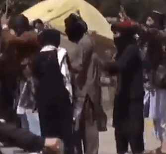 A Taliban fighter strikes a woman with a cane