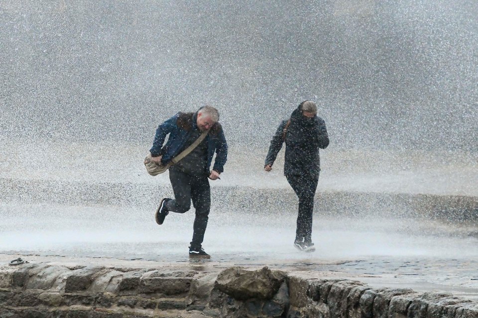 A couple making a dash for it as they walk along the Cobb Harbour at Lyme Regis in Dorset