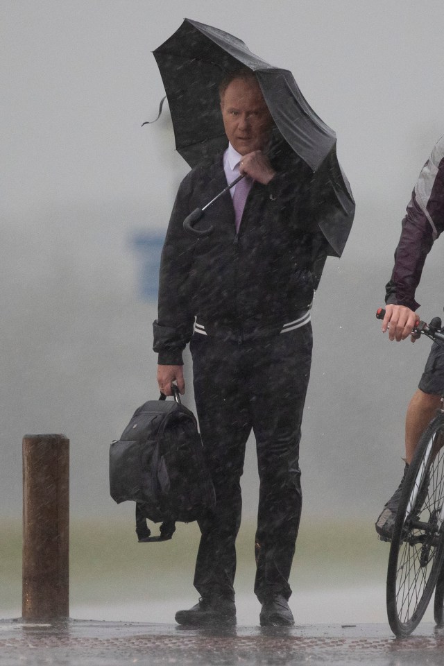 A man shelters under an umbrella during heavy rain on Blackheath Common, south east London