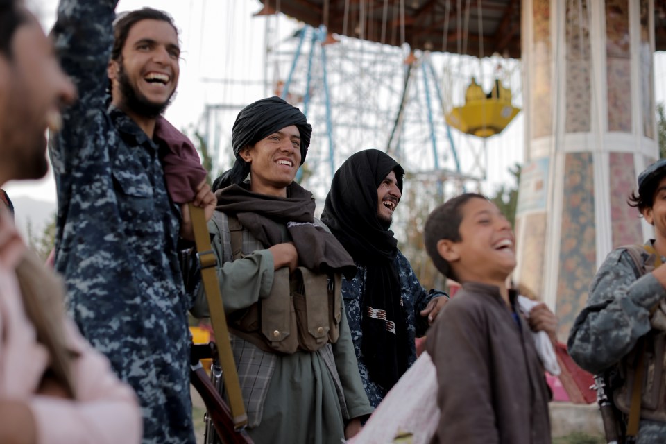 Taliban fighters cheer and laugh as they stand near a carousel