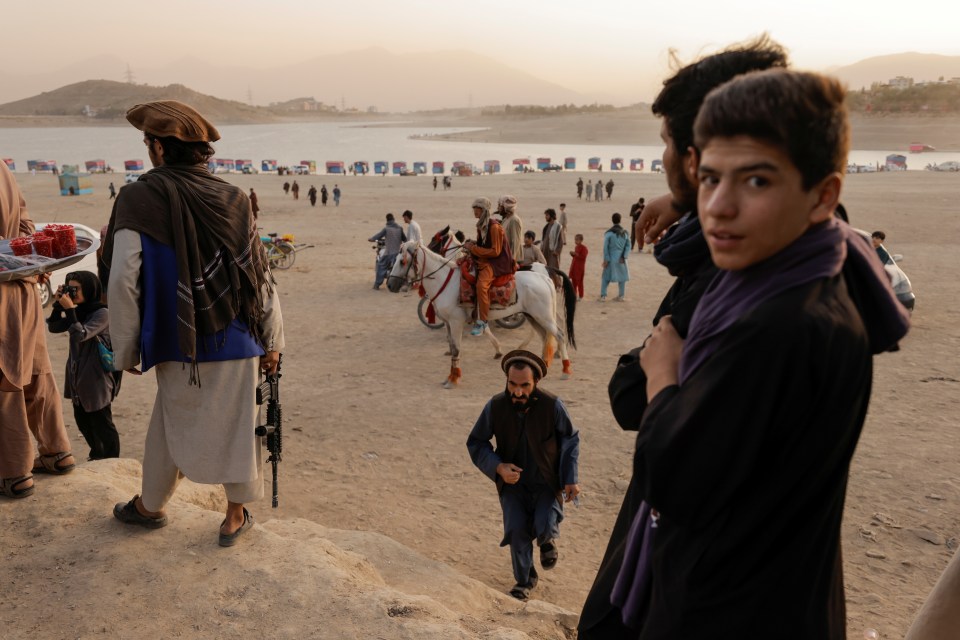 Taliban fighters enjoy treats from a tray alongside some youngsters